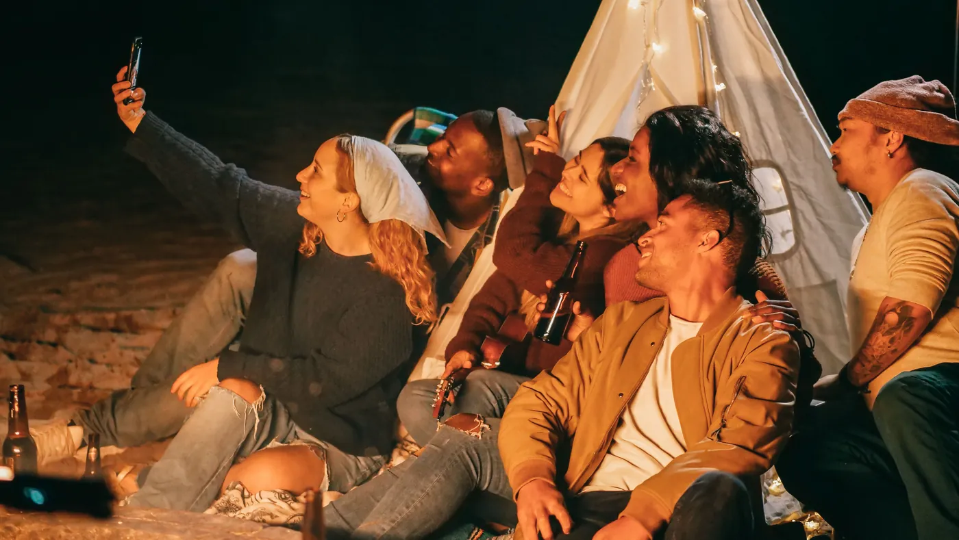 Unos amigos reunidos alrededor de una hoguera en la playa se hacen un selfi.
